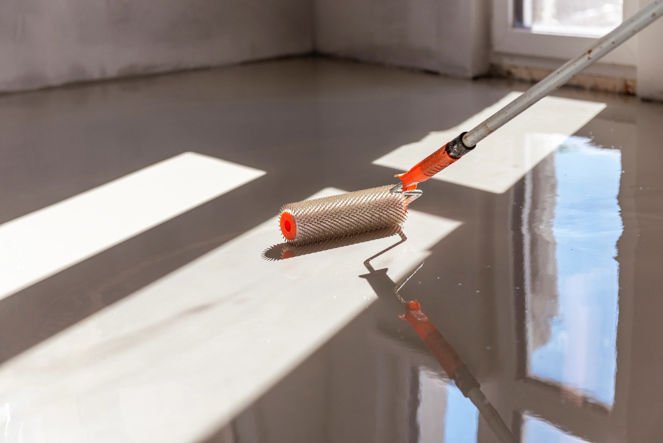 Applying low VOC epoxy and urethane floor coating with a textured roller in a commercial space.