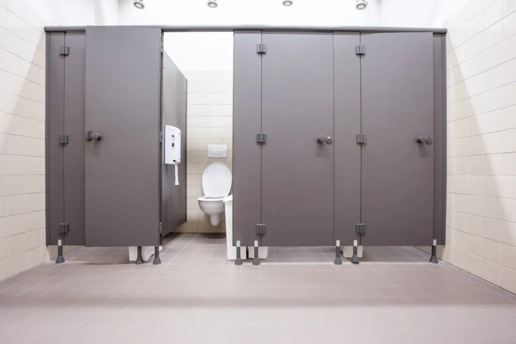 Public restroom featuring gray toilet partitions and tiled floors built to withstand moisture, frequent cleaning, and heavy daily use.